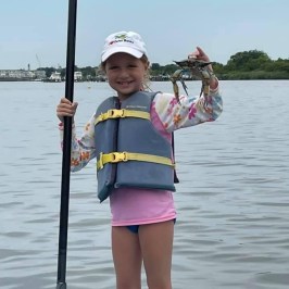 a little girl standing next to a body of water