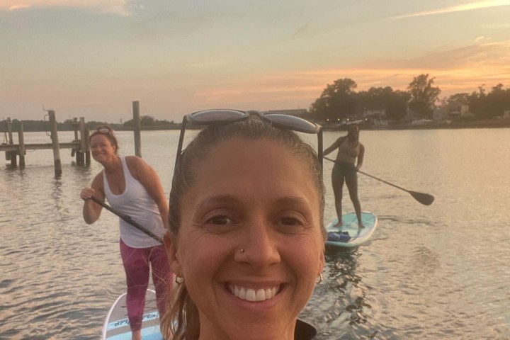 a woman standing next to a body of water posing for the camera