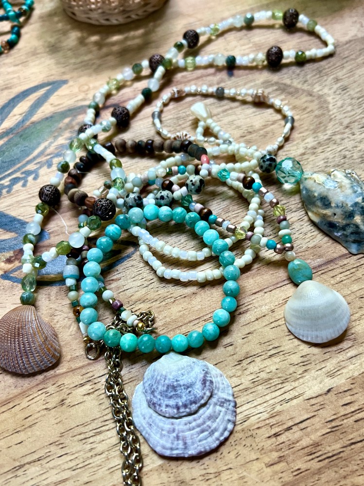 Colorful bead necklaces and seashells on a wooden surface.